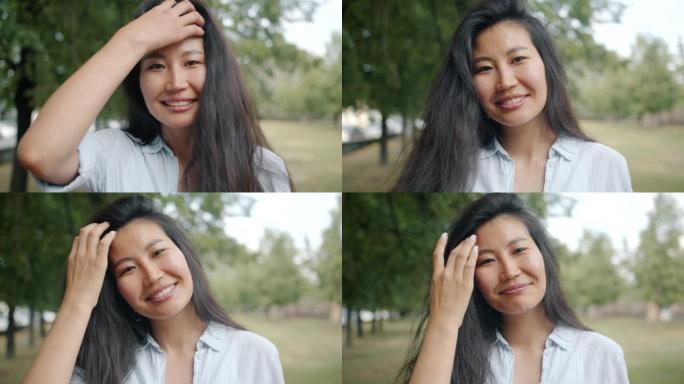 亚洲妇女在公园里看着相机微笑触摸头发的特写肖像