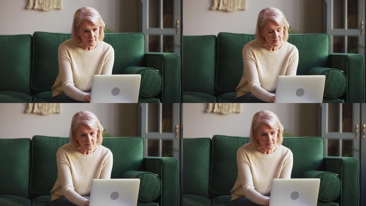 坐在沙发上的笔记本电脑上打字的严重老年成熟女人