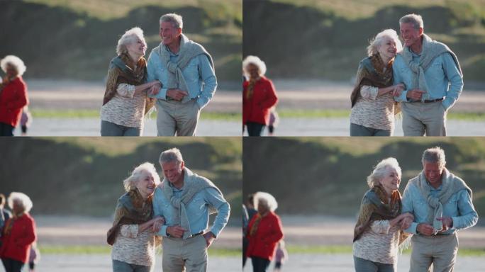 热爱活跃的老年夫妇在寒海滩度假时手挽手走在海岸线上