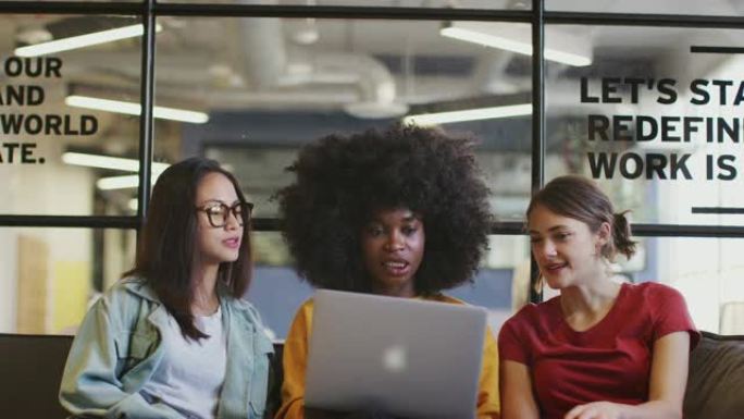三名千禧一代女性在办公室休息室的一次休闲会议中，一起使用笔记本电脑，倾斜镜头