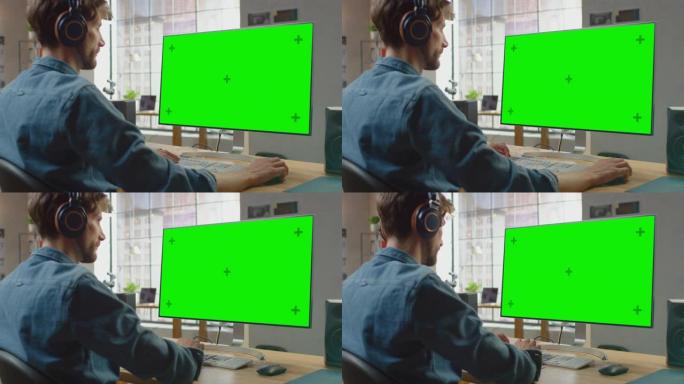 年轻的专业创意员工在他的个人计算机上工作，并带有绿色大屏幕模拟显示屏。他在一个很酷的办公室阁楼里工作