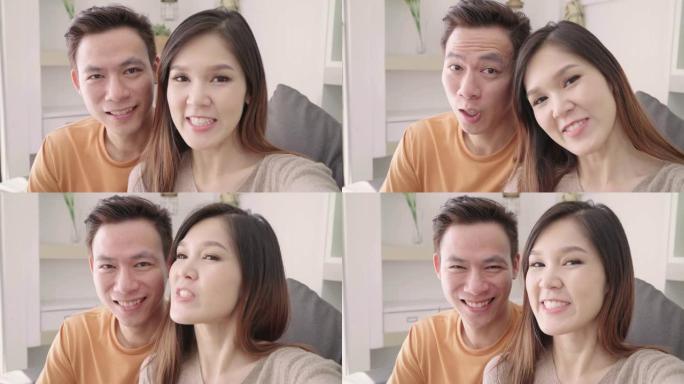 亚洲夫妇在家里的客厅与朋友使用智能手机视频通话，甜蜜的夫妇在家放松时躺在沙发上享受爱情时刻。生活方式