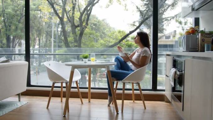 拉丁美洲妇女一边吃早餐，一边看窗户。