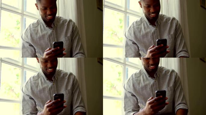 在一个舒适的家庭4k中，年轻黑人使用智能手机坐在窗台上的前视图
