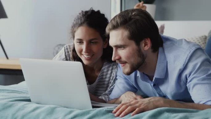 幸福的夫妇使用笔记本电脑观看在线节目躺在床上