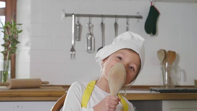 一个打扮成专业厨师的小女孩在厨房里用木勺作为麦克风唱歌。