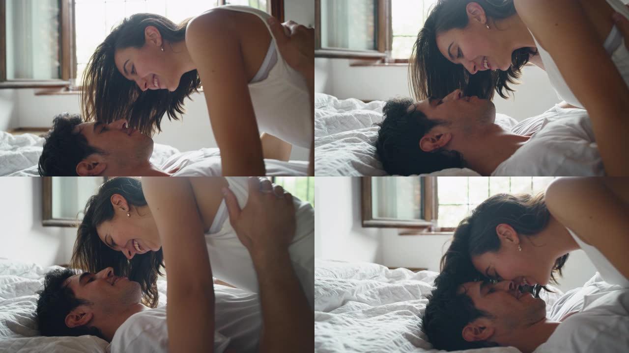 年轻的新婚夫妇穿着睡衣的慢动作在阳光明媚的清晨在卧室里玩耍和接吻