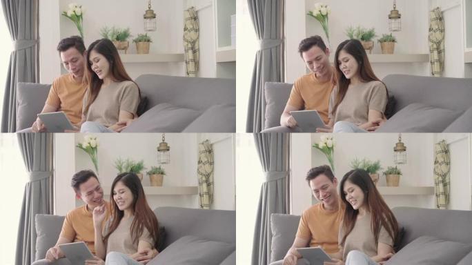 亚洲夫妇在家中客厅使用平板电脑在互联网上进行在线购物，甜蜜的夫妇在家中放松时躺在沙发上享受爱情时刻。