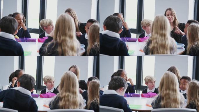 小学生坐在桌子旁吃盒装午餐并与老师交谈