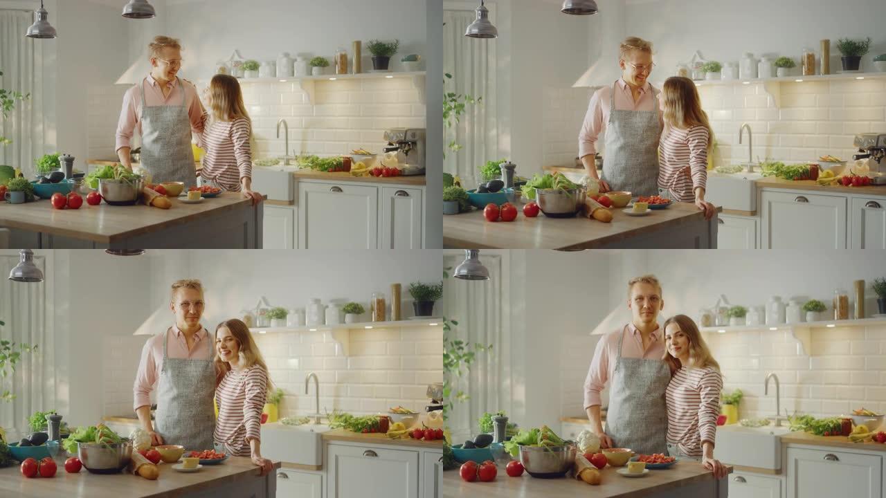 戴着围裙的英俊年轻男子和漂亮的女孩正在厨房里准备沙拉。幸福的夫妻互相拥抱。天然清洁饮食和健康的生活理