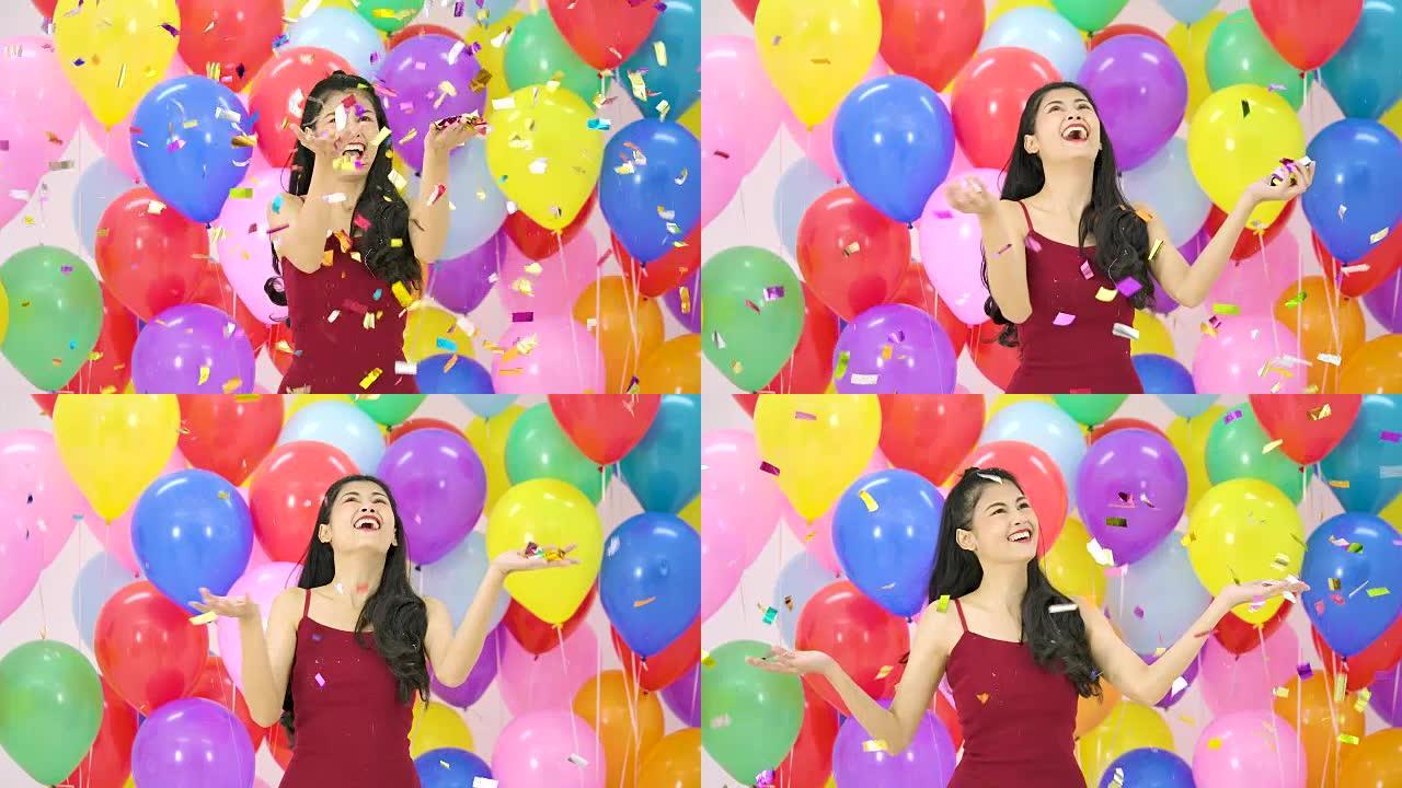 美丽的亚洲女人在派对上以慢动作带着快乐的情感跳舞，彩色气球背景。