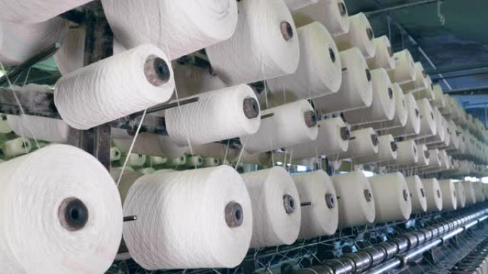 纺织厂机器线轴在机架上与纤维一起切割。纺织厂设备在工作。