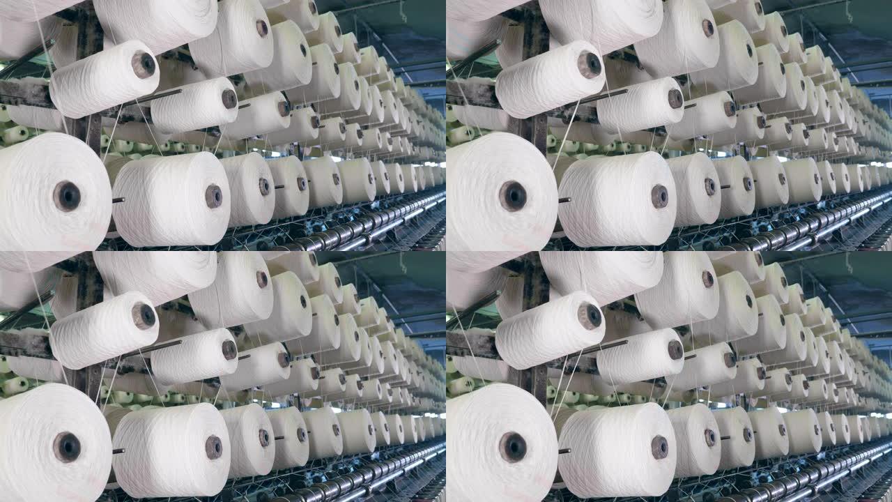 纺织厂机器线轴在机架上与纤维一起切割。纺织厂设备在工作。