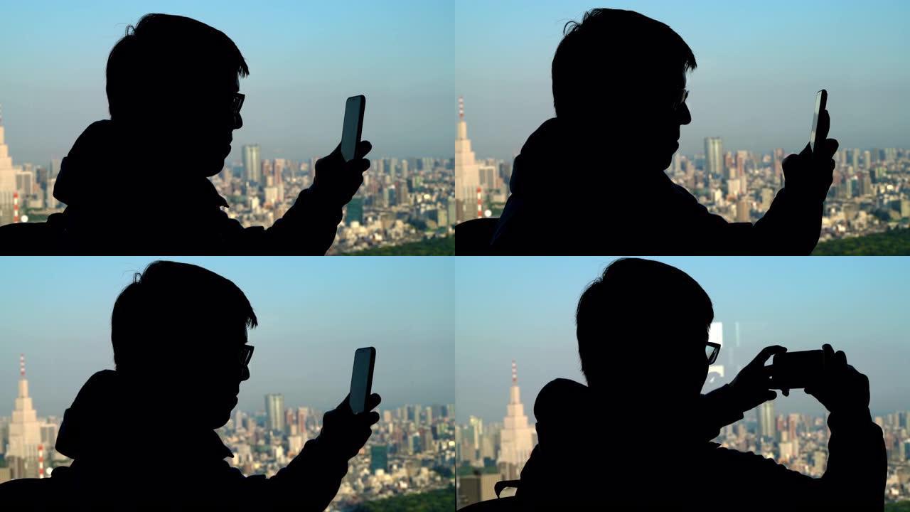 剪影亚洲男子通过智能手机拍摄东京城市景观的照片