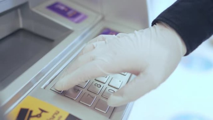 戴着手套的手在自动取款机上按下按钮取钱。冠状病毒大流行期间的保护和安全概念，新型冠状病毒肺炎