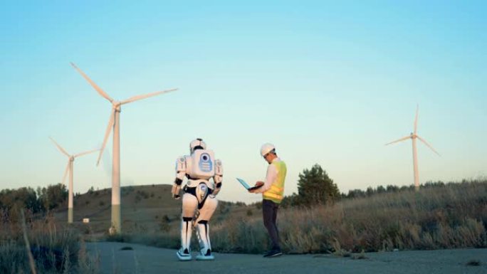 一个类似人类的机器人和一个男性操作员正在沿着一组风车行走