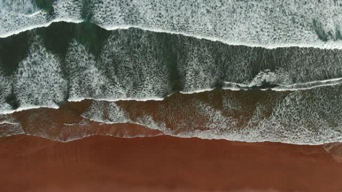 海洋海岸背景。泡沫状的碧绿海浪来到棕色的沙滩上。自上而下的镜头，UHD