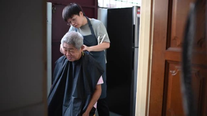由于旅行禁令，一名亚洲华裔中年妇女正在厨房为父亲剪头发和修剪头发