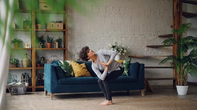 漂亮的年轻女士正在家里训练瑜伽椅子姿势，站在现代公寓的地板上。个人实践，青年和房屋概念。