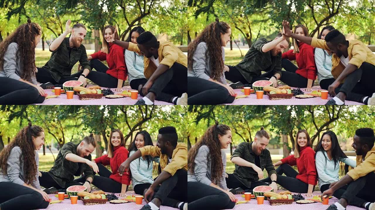 非洲裔美国人和白种人的慢动作在野餐时坐在毯子上，而女孩在说笑。沟通和友谊的概念。