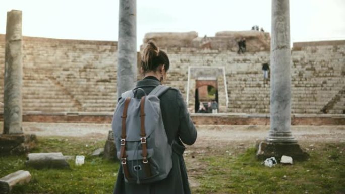 专业旅行博客作者女孩的背景图，带相机拍摄意大利奥斯蒂亚的古代露天剧场柱子。