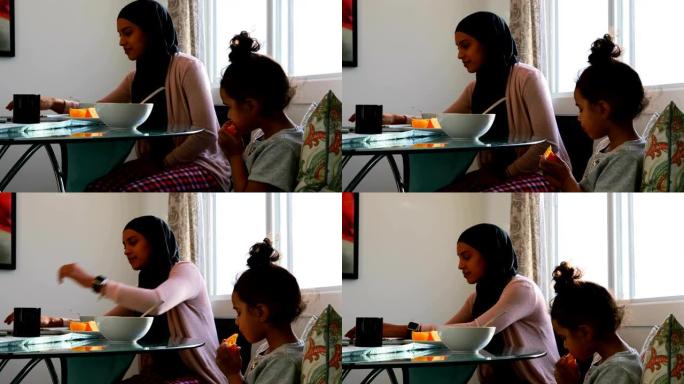 年轻的母亲在女儿在家吃水果时使用笔记本电脑4k