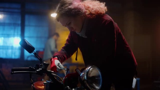 年轻漂亮的女机械师正在修理一辆定制的摩托车。穿着方格衬衫的天才女孩。她用棘轮扳手。创意正宗车间车库。