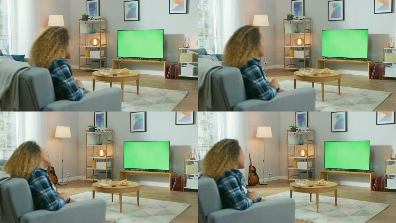 女孩坐在家里坐在沙发上，看着绿色色度键屏幕，放松。男人在舒适的房间里看体育比赛，新闻，电视节目或电影