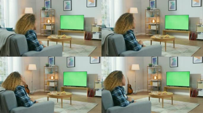 女孩坐在家里坐在沙发上，看着绿色色度键屏幕，放松。男人在舒适的房间里看体育比赛，新闻，电视节目或电影