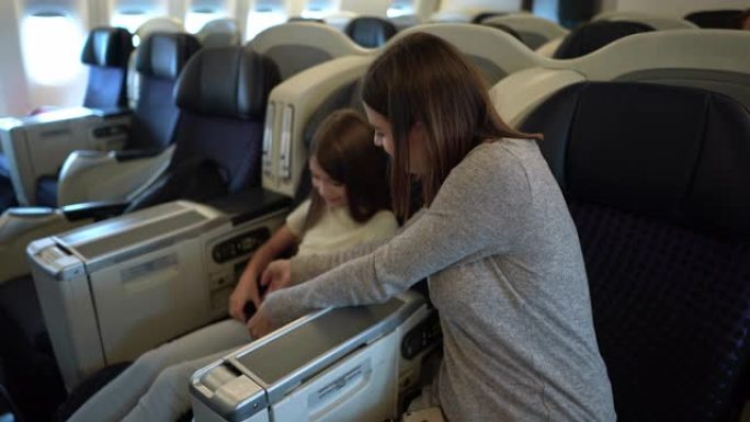 慈爱的妈妈在起飞前在飞机上帮助女儿系好安全带