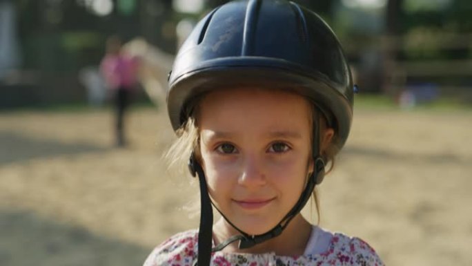 在阳光明媚的日子里，一个戴着骑师头盔的小女孩在镜头前微笑的真实照片