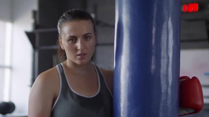女拳击手在健身房训练后在沉重的袋子附近摆姿势