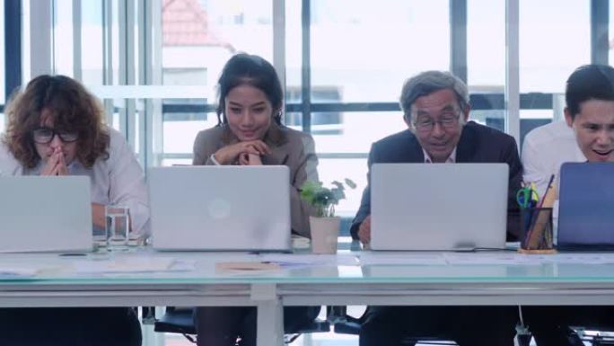 一群商业团队和资深人士看着电脑，在创业办公室庆祝成功的同时快乐。商业，人，成功，获胜的概念。人们庆祝