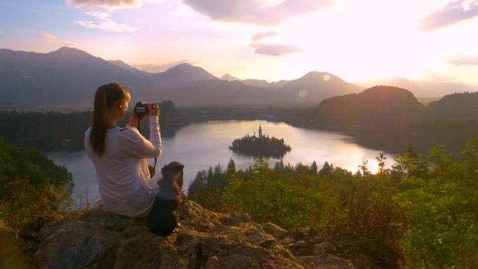 复制空间: 旅行者女孩坐在她的小狗旁边，拍摄日落照片。