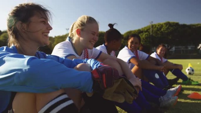 快乐的多元化女足球运动员坐在足球场上聊天。4k