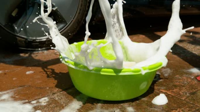 特写: 洗车的人将海绵滴入装满肥皂水的水桶中