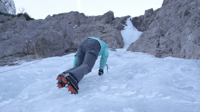 自下而上: 女人爬冰停下来，抬头看着美丽的冰冻瀑布。