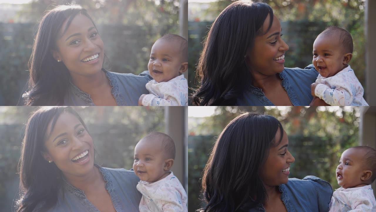 微笑的非洲裔美国母亲拥抱并在花园里与小女儿玩耍的肖像