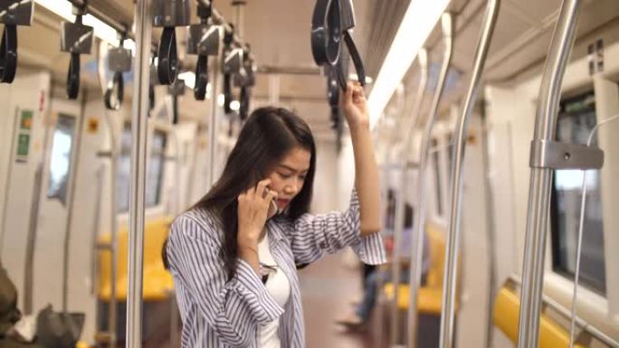 亚洲妇女在地铁上通过电话交谈