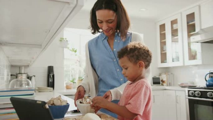 千禧一代的母亲和蹒跚学步的儿子在厨房里一起准备食物，侧视图，特写
