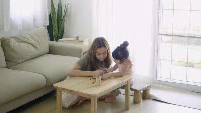 快乐的亚洲女孩和妈妈在家里的客厅用蜡笔画画。