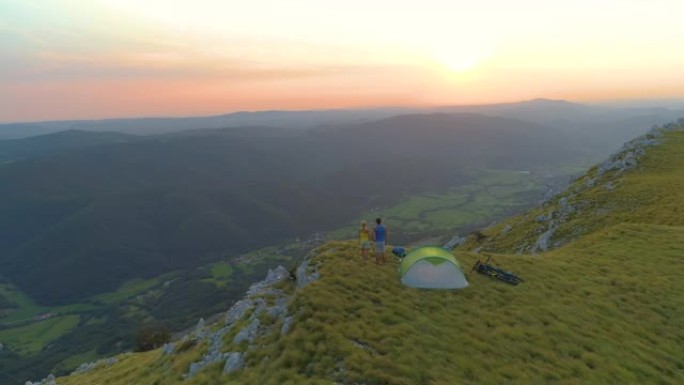 无人机: 活跃的情侣站在山边看日落。
