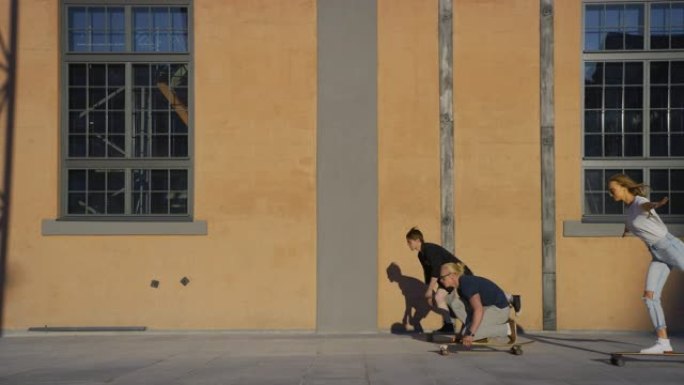 一群时尚的女孩和男孩以各种有趣的姿势骑在滑板上。在工业仓库的背景黄色墙壁上。慢动作侧视摄像机拍摄