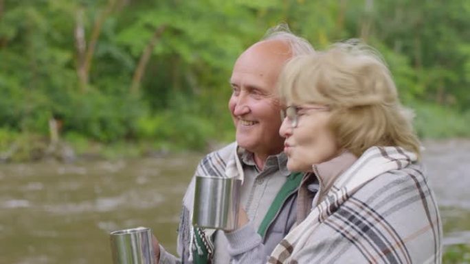 幸福的老年夫妇在河岸上喝热茶