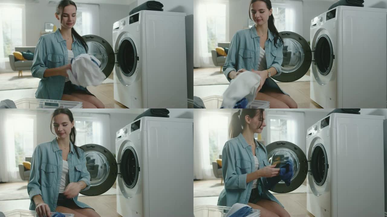 美丽微笑的黑发年轻女子穿着家常牛仔裤坐在洗衣机前。她给洗衣机装上脏衣服。明亮宽敞的客厅，室内现代。