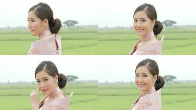 穿着传统东南亚服装的迷人亚洲女性的特写肖像转头对着镜头，在泰国稻田的背景下微笑。