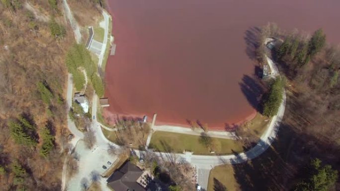 无人机: 在空旷的道路上飞行，绕着充满红色水的湖泊奔跑。