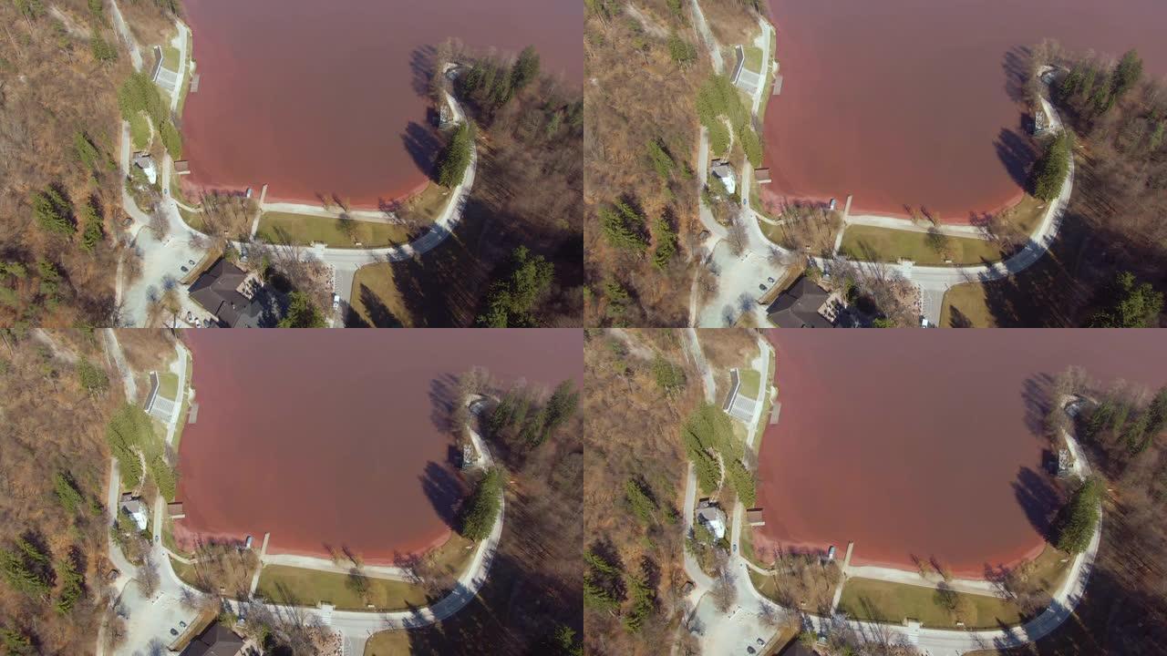 无人机: 在空旷的道路上飞行，绕着充满红色水的湖泊奔跑。
