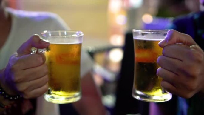 4k慢动作镜头，两个亚洲男子敬酒和碰杯啤酒，在酒吧和餐厅一起欢呼，放松和喝酒的概念