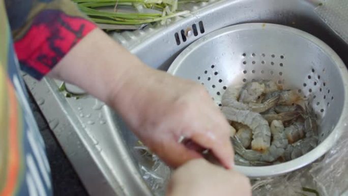 亚洲高级妻子在家里的厨房里为晚餐洗新鲜虾